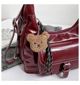 Detail of burgundy leather handbag featuring white contrast stitching and teddy bear charm