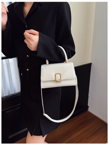 Detail of white crocodile pattern handbag with gold clasp and adjustable strap on model