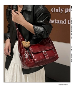 Detail of burgundy vintage tote bag with glossy leather texture and small plush bear charm
