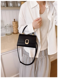 Detail of black crocodile embossed baguette bag with golden clasp on a kitchen counter