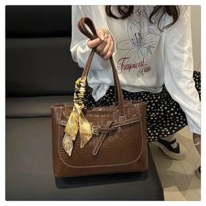 Detail of coffee brown crocodile pattern tote bag with decorative silk scarf on handle