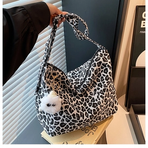 Detail of leopard print canvas tote bag featuring wide strap and plush white charm