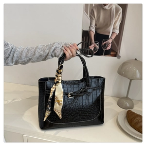 Detail of black croc-embossed tote bag with white stitching and printed silk scarf