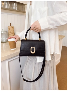 Detail of black crocodile-embossed mini bag with golden oval lock and sturdy top handle