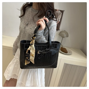 Close-up of black crocodile pattern tote bag with decorative scarf and metal buckle detail