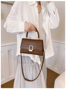 Detail of dark brown faux crocodile texture handbag with elegant gold metal buckle