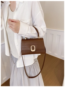 Brown crocodile embossed handbag with golden oval clasp shown in a lifestyle setting
