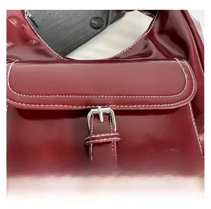 Detailed close-up of dark red glossy leather bag with white contrast stitching and silver buckle