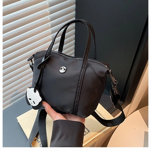 Detail of black nylon dumpling bag featuring an adjustable strap and a panda charm accessory