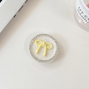 Detail of round phone grip with yellow bow and rhinestones on a clean desk