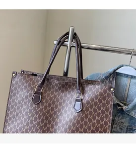 Detail of dark brown tote bag with M-pattern monogram print and gold metal buckles