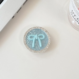 Close-up of light blue round phone grip with a 3D bow and sparkling rhinestones