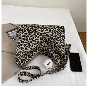 Detail of leopard print canvas bag featuring a white plush cat charm and adjustable strap