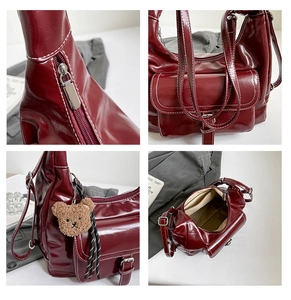 Detail view of burgundy leather tote bag with white stitching and plush bear charm