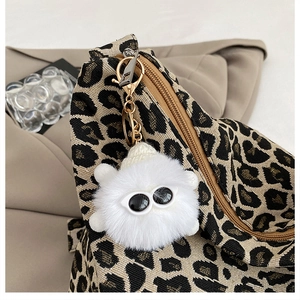 Close-up of a white fluffy keychain charm with sunglasses on a leopard print canvas bag