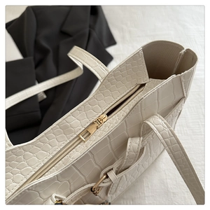 Close-up of white crocodile embossed tote bag texture with golden zipper hardware