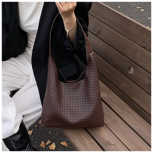 Dettaglio della borsa tote in pelle intrecciata marrone scuro su una panca di legno