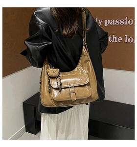 Detailed close-up of brown tote bag with buckle pocket and plush bear pendant detail