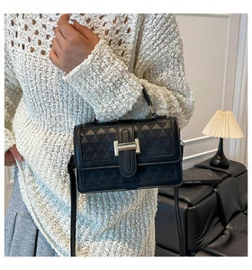 Close-up of black quilted leather handbag with gold H-shaped buckle and fine strap