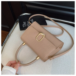 Close-up of beige crocodile pattern handbag with gold clasp on a minimalist chair