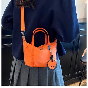 Detail of vibrant orange nylon dumpling bag featuring a cute panda charm and wide strap