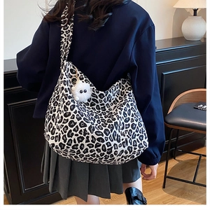 Detail of leopard print canvas bag with furry pendant shown from a side-back view