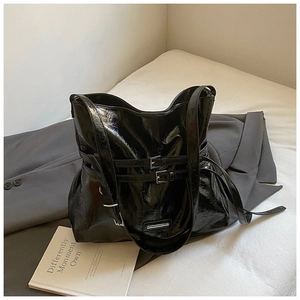 Detail of a large black glossy tote bag with metal buckles on a white bed sheet