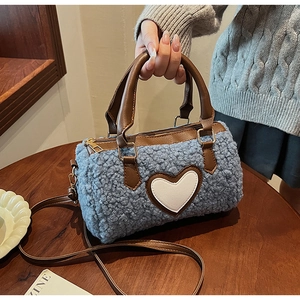 Detail of blue plush cylinder bag featuring white heart patch and brown leather handles