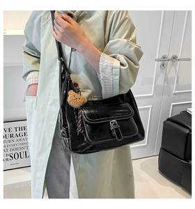 Detail of black glossy shoulder bag with white topstitching and cute brown bear charm
