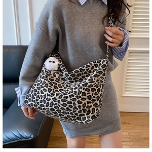 Detail of large leopard print crossbody bag with white plush charm worn by model