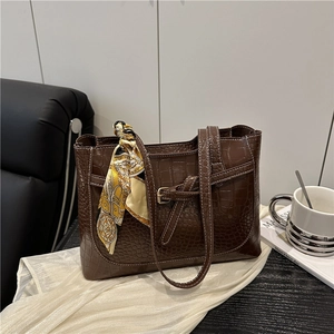 Brown crocodile pattern tote bag with decorative silk scarf on a sleek leather sofa