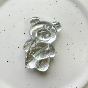 Close-up of a transparent 3D bear crystal phone grip on a white ceramic plate