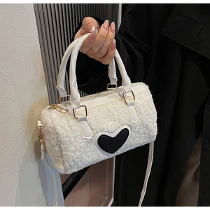 Detail of white faux shearling pillow bag featuring a black heart patch and gold hardware