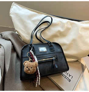 Detail of black leather tote bag featuring a cute plush bear pendant and metal zipper