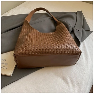 Dettaglio della borsa tote marrone intrecciata con tracolla larga su sfondo di tessuto bianco