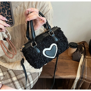 Close-up of black fuzzy faux shearling pillow bag with heart patch in a cozy autumn setting