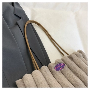Détail d'un sac cabas en peluche montrant la texture rayée et l'écusson décoratif