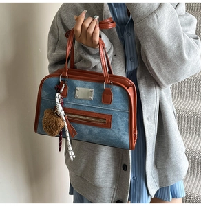 Detail of blue denim Boston bag with brown leather trim and a cute teddy bear charm