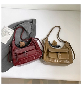 Detail view of burgundy and khaki hobo bags with white stitching and bear charm