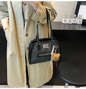 Close-up of retro black tote bag with silver zipper and decorative brown plush bear charm