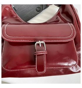 Detail of burgundy glossy leather shoulder bag with white contrast stitching and buckle