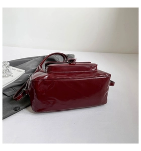 Close-up of deep red patent leather shoulder bag with white contrast stitching detail
