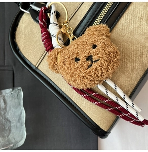 Macro detail of plush bear charm with woven ropes on a vintage canvas underarm bag