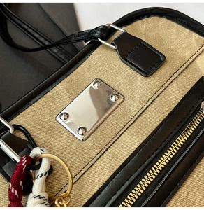 Macro detail of canvas texture with black leather trim and silver metal plate on handbag