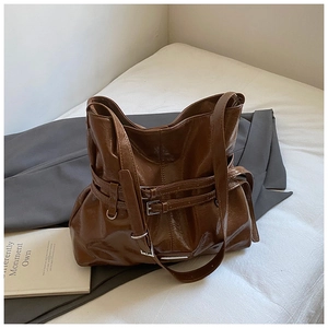 Brown faux leather tote bag with decorative belts on a white bed lifestyle scene