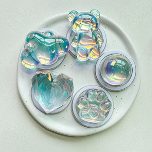 Detailed view of iridescent aurora phone grips in bear, heart, and paw shapes on stone