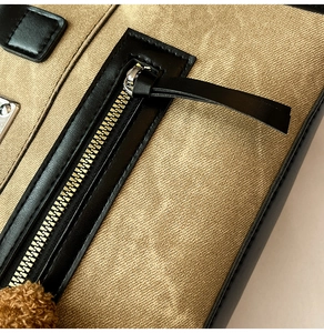 Detailed close-up of khaki canvas tote with black leather trim and silver metal zipper