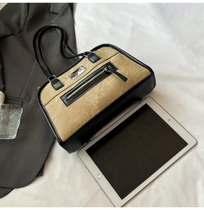 Detail of tan suede tote bag with black trim, zipper pocket, and metallic plate