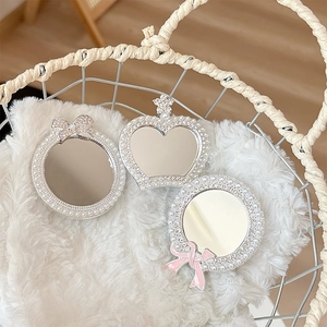 Mini handheld mirror set with pearls and rhinestones on a white plush background
