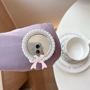 Detail of a pearl and crystal inlaid circular mirror phone stand with a pink bow accent
